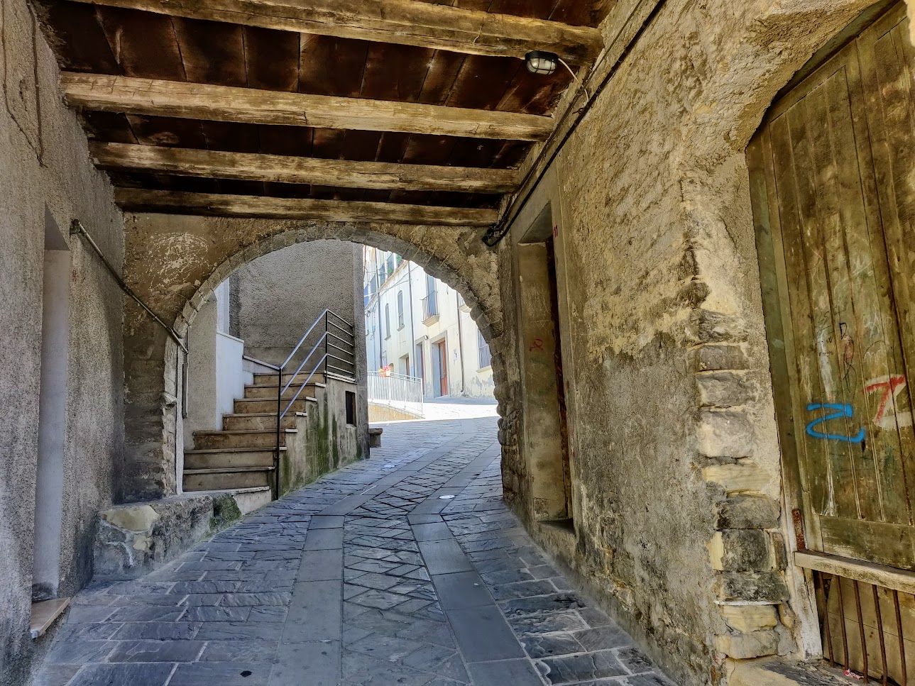 Un arco in pietra con travi di legno e una strada lastricata in un borgo lucano